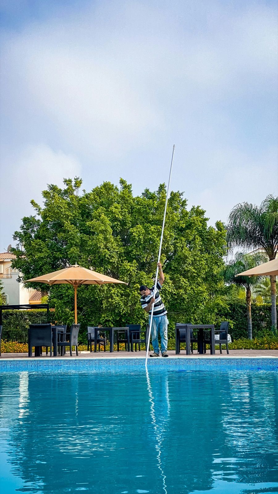 Pool technician skimming a backyard pool with a long pole